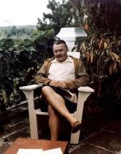 Ernest Hemingway sitting on a deck chair with a book at his home, Finca Vigia, San Francisco de Paula, Cuba.